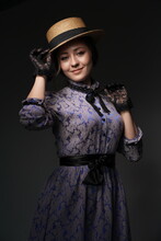 A Girl In A Blue Retro Dress In The Style Of The 1900s. A Woman Adjusts Her Hat In Lace Gloves. Historical Fashion Of The 19th Century. High Quality Photo