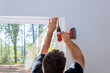© ungvar - Professional technician is screwing the fastenings on the windows of newly constructed home to install blinds on them