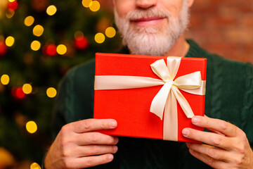 an elderly man in a green knitted with gift box near the Christmas tree