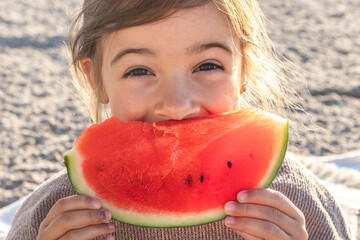 Close-up, little girl eats watermelon on the beach.