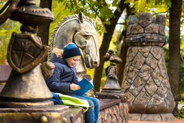 happy child sits on a bench and reads a book. a happy boy reads a textbook on a bench in Presnensky Park.