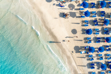 Canvas Print - Top view of beautiful sandy popular beach La Pelosa with turquoise sea water and colorful blue umbrellas on the Sunset, Islands of Sardinia in Italy, aerial drone shot