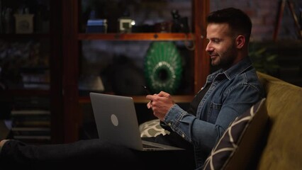 Sticker - Businessman working from home on laptop computer. Happy young man sitting on couch in home office with laptop.