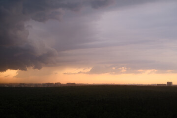 Wall Mural - Stormy sky at sunset with dark rain clouds. Rain over a summer forest with green trees