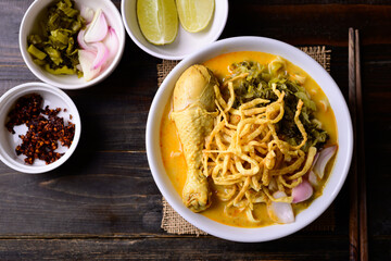 Wall Mural - Northern Thai food (Khao Soi), Spicy curry noodles soup with chicken on wooden background, Local Thai food