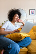 © Daniel - Happy African American woman having fun using laptop at home. Laughing watching funny online videos.