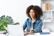 © PaeGAG - Cheerful african american woman using laptop while sitting on chair in living room