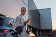 © Halfpoint - Businessman holding smartphone while charging car at electric vehicle charging station, closeup.