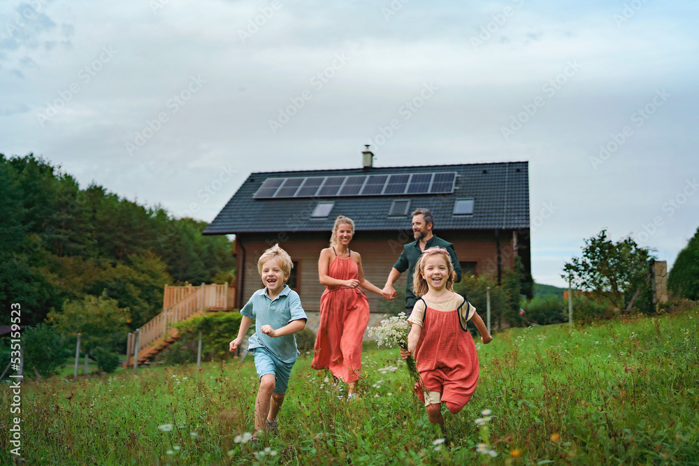 Happy family running near their house with solar panels. Alternative energy, saving resources and sustainable lifestyle concept.