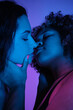© Clique Images - Vertical close-up studio shot of attractive young African American and Caucasian women in love standing in neon light kissing each other