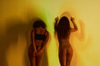 © Clique Images - Horizontal rear view medium long studio shot of two ethnically diverse women wearing lingerie standing in yellow projector light