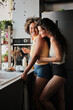 © Clique Images - Vertical medium long shot of Black and Caucasian women in love spending morning together in kitchen at home flirting and hugging