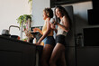 © Clique Images - Low angle view medium long shot of young lesbian couple spending morning at home standing at kitchen counter laughing at something