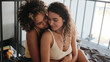 © Clique Images - High angle view medium close-up shot of two young women sitting together on bed in morning embracing and flirting