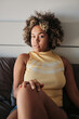 © Clique Images - Vertical medium portrait of attractive young Black woman sitting relaxed on bed in morning looking at camera