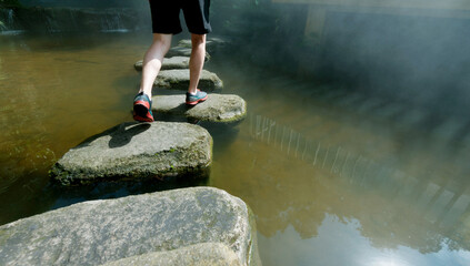 Wall Mural - Man walking crossing a river on stones