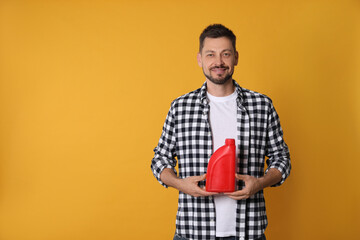 Wall Mural - Man holding red container of motor oil on orange background. Space for text