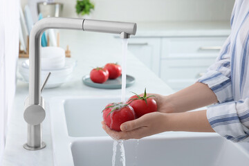 Poster - Woman washing fresh ripe tomatoes under tap water in kitchen, closeup