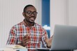 © VK Studio - Smiling puzzled african american man reading email with news, working at laptop, spreading hands