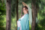 Young beautiful Asian woman wear dressing in traditional Chinese costume ancient fashion style warrior style with ancient word on in nature outdoor with green nature of park background.