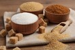 Different types of sugar in granules and cubes on wooden table, closeup