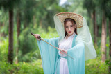 Young beautiful Asian woman wear dressing in traditional Chinese costume ancient fashion style warrior style with ancient word on in nature outdoor with green nature of park background.
