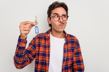 Young hispanic man holding home keys isolated on white background confused, feels doubtful and unsure.