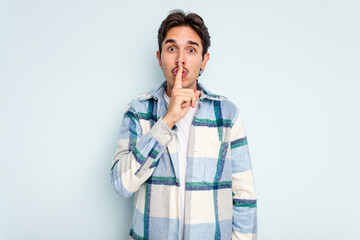 Young hispanic man isolated on blue background keeping a secret or asking for silence.