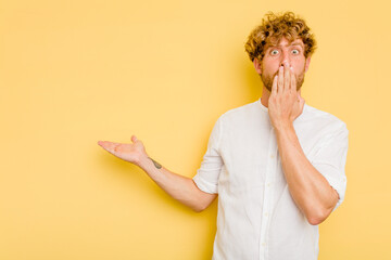 Wall Mural - Young caucasian man isolated on yellow background impressed holding copy space on palm.