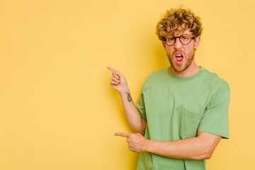 Wall Mural - Young caucasian man isolated on yellow background pointing with forefingers to a copy space, expressing excitement and desire.