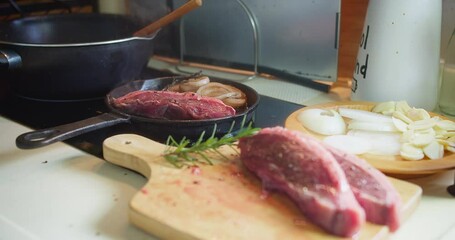 Wall Mural - Close up cooking meat beef steak on a hot grill pan with herbs in the kitchen, preparing barbeque grilling food at home