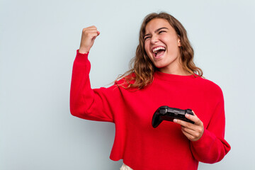 Young caucasian gamer woman holding a game controller isolated on blue background raising fist after a victory, winner concept.