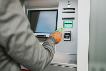 Handsome middle age businessman with eyeglasses standing on city street and using ATM machine to withdraw money from credit or debit card. Hand close up.