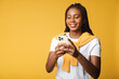 Cheerful attractive brunette woman holding smartphone, enjoying chatting in social networks, texting messages and smiles, using mobile app for dating on the phone, isolated on yellow, copy space