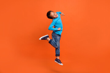 Ful body photo of cute small schoolboy jumping have fun playful fooling dressed stylish blue outfit isolated on orange color background