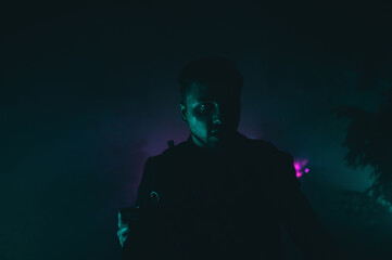 Night cinematic portrait of a man at night in colored light on a background of foggy view.