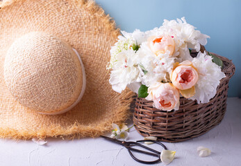 Wall Mural - Summer concept. Hat and basket with romantic summer roses and peonies flowers  against blue background. Selective focus. Still life.