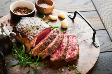 Steaks. Sliced grilled meat steak New York or Striploin with spices rosemary and pepper on black marble board on old wooden background. Top view. Mock up.