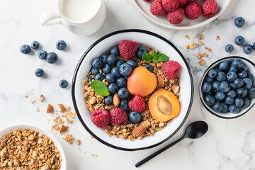 Wall Mural - Fruit and berry granola bowl on white marble background. Delicious healthy vegetarian breakfast bowl