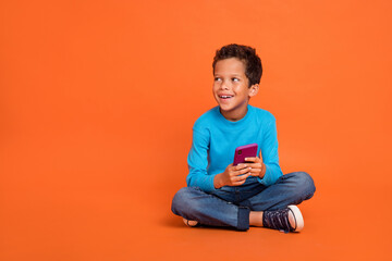 Canvas Print - Full body photo of cute small boy hold gadget influencer look empty space dressed stylish blue outfit isolated on orange color background