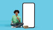 Pensive black student guy sitting next to big blank smartphone