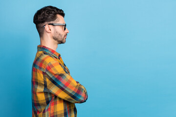 Wall Mural - Side profile photo of young stylish smart man wear plaid shirt eyeglasses arms folded look empty space isolated on blue color background