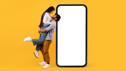 Wall Mural - Loving indian couple posing near big blank smartphone with white screen