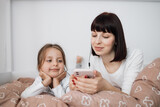 Fototapeta  - Close up of smiling mom and little daughter relax in cozy bed read funny interesting children book together, happy mother and small preschooler girl child enjoy fairytale rest in comfortable bedroom
