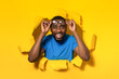Excited black man taking off eyeglasses and smiling at camera, standing in torn yellow paper hole
