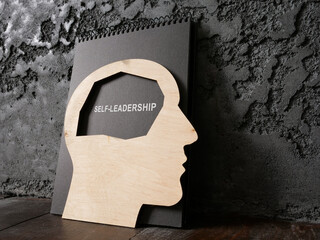 Head and notepad with sign self-leadership near wall.