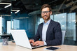 © Liubomir - Portrait of mature boss inside office with laptop, successful and satisfied investor manager looking at camera and smiling man in glasses and business suit, investor with beard sitting on chair