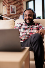 Poster - Young adult working and listening to music on headphones, using laptop to send email and do research data work. Analyzing business report on computer and listening to podcast show.