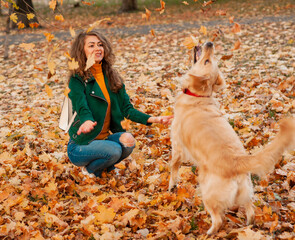 Wall Mural - Closeup of curly woman sitting with her dog in autumn leaves outdoors