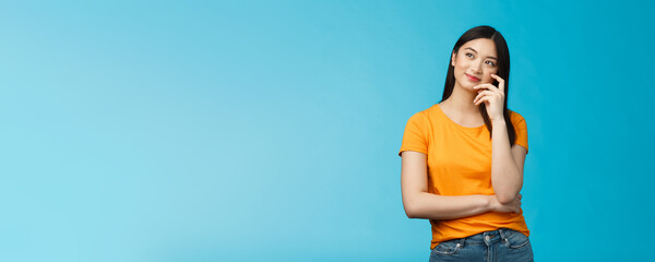 Wall Mural - Joyful confident asian girl with dark haircut tilt head, dreaming, imaging interesting plan, smiling cunning, have idea, thinking and making choice, look up thoughtful, stand blue background